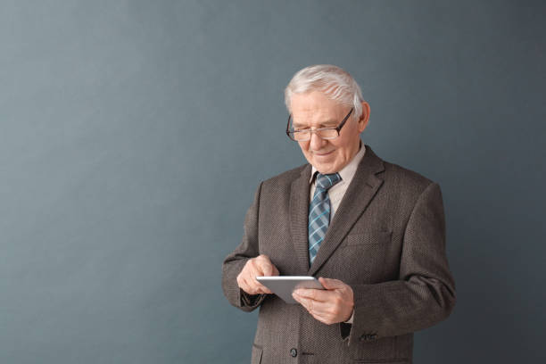 istock Senior man teacher wearing glasses studio standing isolated on gray using internet on digital tablet concentrated 1170400558