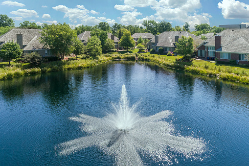 Aerial view of a townhouse complex with a pond and fountain in a Chicago suburban neighborhood in summer.