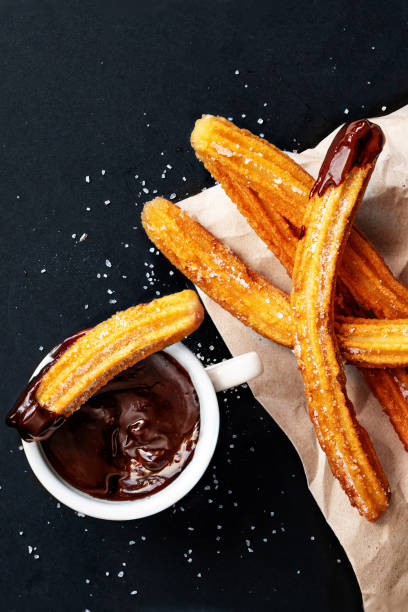 istock Churros with sugar dipped in chocolate sauce on a black background. Churro sticks. Fried dough pastry, top view 1170417258