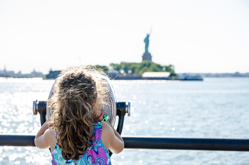 Kid looking at Statue of Liberty through paying binoculars from the Liberty State Park in Jersey city during summer day