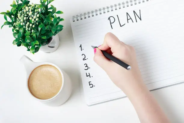 Photo of Female hand writes a plan in a notebook, goal setting concept