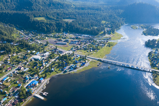 Aerial view of the road bridge connecting the two banks of the Biya River on which the two villages of Iogach and Artybash are located at mouth of the Teletskoye Lake, the sun is reflected in water.