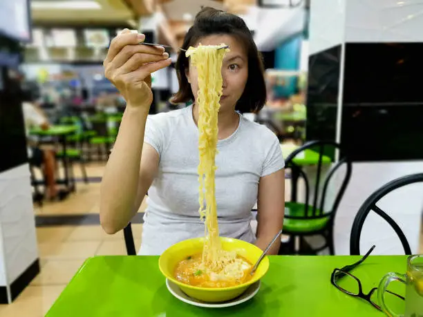A woman is holding fork and pulling instant noodles high in the air.
