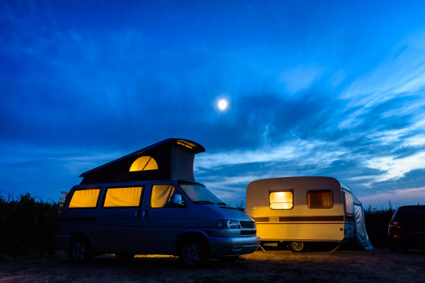 キャンピングカーとキャラバンは、嵐の空の上に月が輝く夕暮れ時に内側から照らされました。 - car stationary blue sky ストックフォトと画像