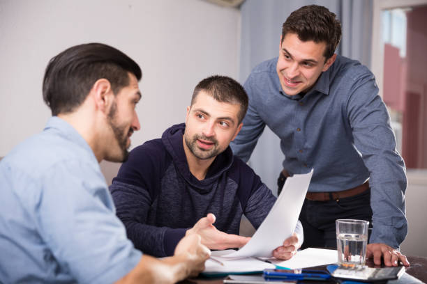 istock Three smiling men discussing papers at desk 1170449511
