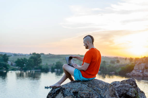 istock A man working on a laptop while sitting on a rock on a beautiful sunset. 1170450447