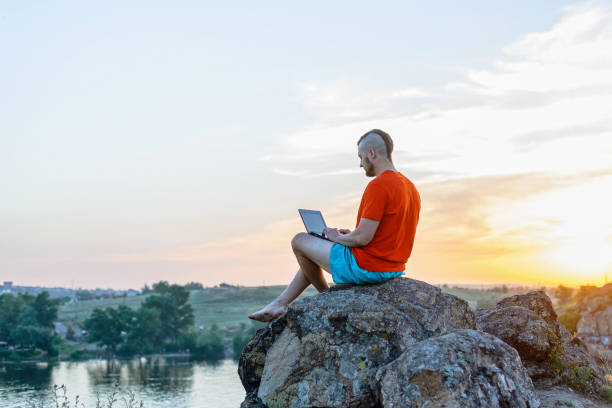 istock Freelancer working on a laptop while sitting on a cliff against the background of a sunset. 1170450452