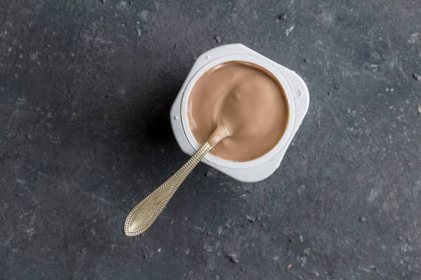istock Chocolate flavoured yogurt in plastic cup with spoon on grey texture background - top view photo of yoghurt cup 1170452362