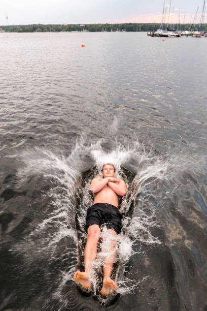 Young man jumps backwards into a lake, water splashes around