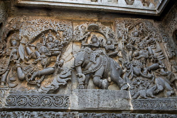 Ornate wall panel reliefs depicting (from left) Garuda carrying Vishnu, Lord Indra and Indrani on elephant Eirawat and Vishnu rescuing Gajendra from crocodile, Hoysaleshwara temple, Halebidu, Karnataka, india. relieves ornamentados del panel de pared que representan (desde la izquierda) garuda llevando a vishnu, lord indra e indrani en el elefante eirawat y vishnu rescatando gajendra de cocodrilo, templo hoysaleshwara, halebidu, karnataka, india.