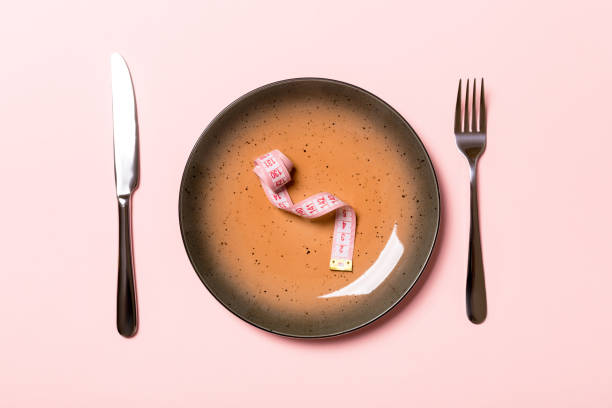 istock Round plate with measure tape inside with fork and knife on pink background. Top view of obesity concept 1170462373