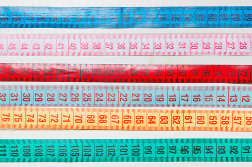 Close up of a group of colorful measure tapes lying in rows as a background. Diet concept on wooden background.