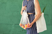 Female hands with shopping cotton mesh eco bag on green background. Zero waste concept