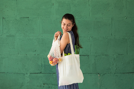 Woman shopping fruits and vegetables with reusable cotton Eco produce bag. Zero waste lifestyle concept