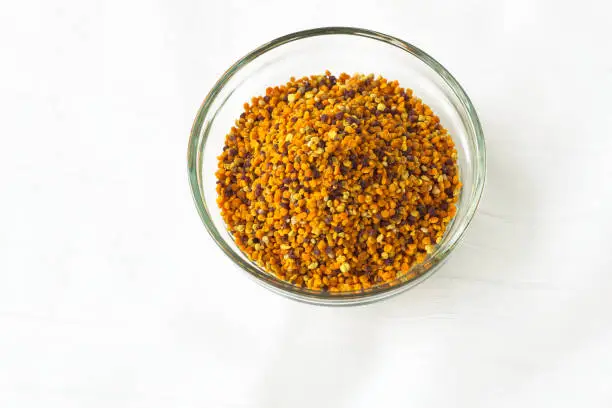Bee pollen granules in a glass bowl on white background.Superfood, mixture of flower nectar, enzymes, honey, wax secretions. Nutrients, amino acids, lipids and vitamins.Flatlay,top view,copy space.