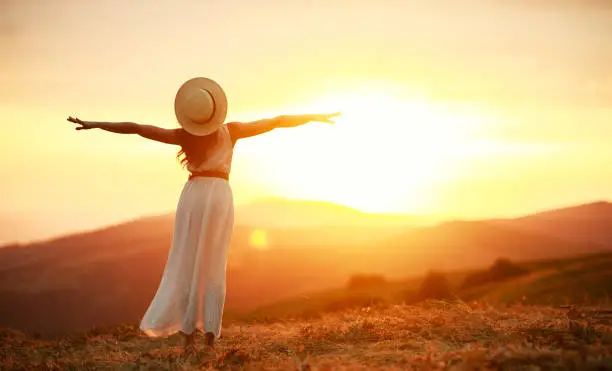 Photo of Happy woman standing with her back on sunset in nature iwith open hands