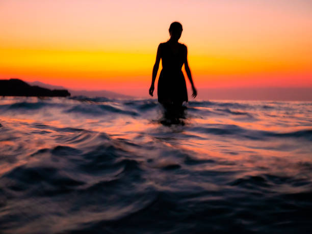 Girl in the sea at sunset Backlight silhouette of girl on the sea at sunset. walking in water stock pictures, royalty-free photos & images