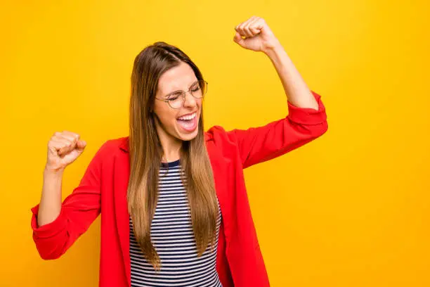 Photo of Portrait of cheerful lady raising her fists screaming shouting yeah wearing red striped shirt isolated over yellow background