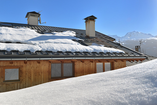 view on a wooden chalet with a zinc roof in spring with the snow melting under clear sky