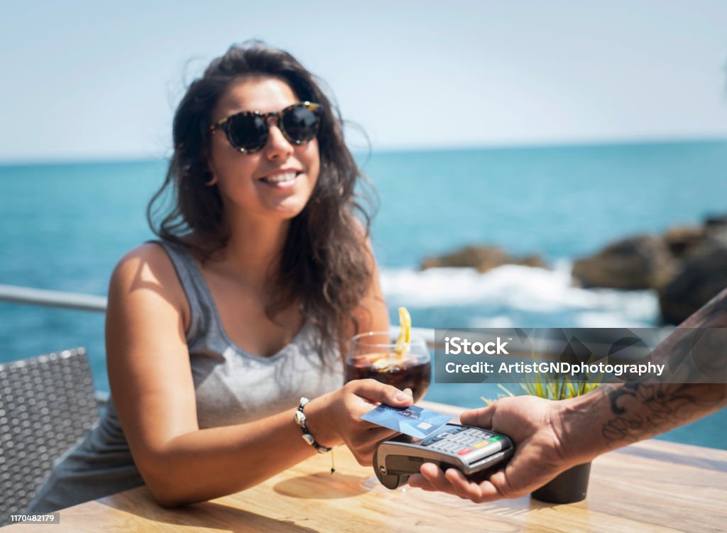 Card payment Beautiful young woman making payment on the beach in luxury summer restaurant, she drinking cold drink in sunny day, smiling Latino woman. Playing Card Stock Photo