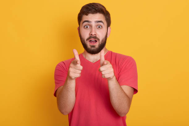 istock Image of handsome young man standing isolated over yellow background, looking at camera and pointing with fore fingers, wearing red casual t shirt, posing with open mouth. People emotions concept. 1170483264