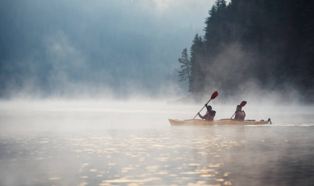 Young couple on kayaking adventure in mountain lake. Couple rowing kayak in beautiful mountain lake at twilight, floating on water with mistycal mood. canoeing stock pictures, royalty-free photos & images