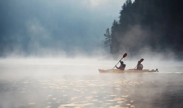Couple rowing kayak in beautiful mountain lake at twilight, floating on water with mistycal mood.