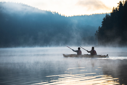 Couple rowing kayak in beautiful mountain lake at twilight, floating on water with mistycal mood.