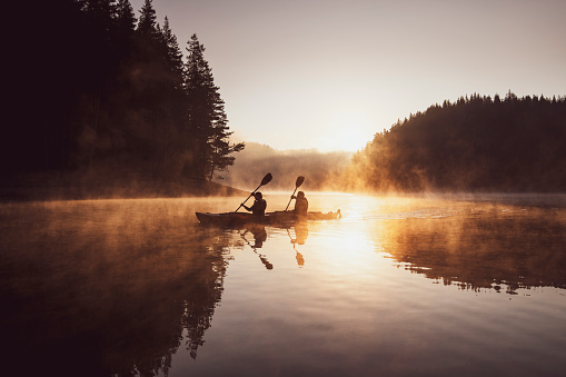 Two people rowing with kayak in lake at beautiful sunrise.