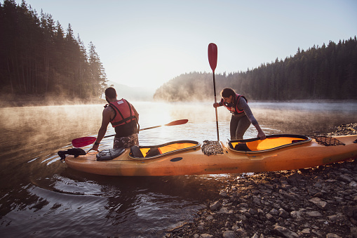 Two people prepare to adventure with kayak in mountain lake.