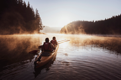 Couple rowing with kayak in lake at beautiful sunrise light.