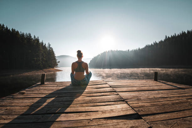Rear view of woman practicing yoga on wooden pier at mountain lake.