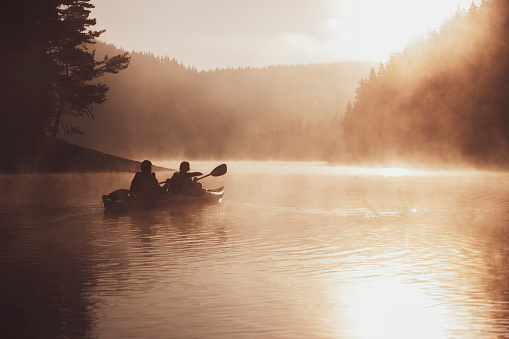 Couple rowing with kayak in lake at beautiful sunrise light.