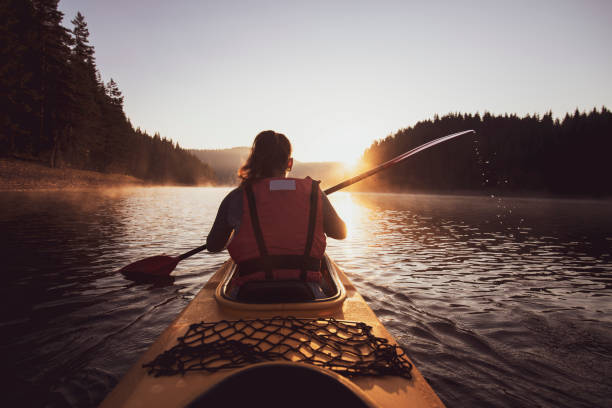 eine frau mit einem kajak bei sonnenaufgang. - kayak canoeing canoe lake stock-fotos und bilder