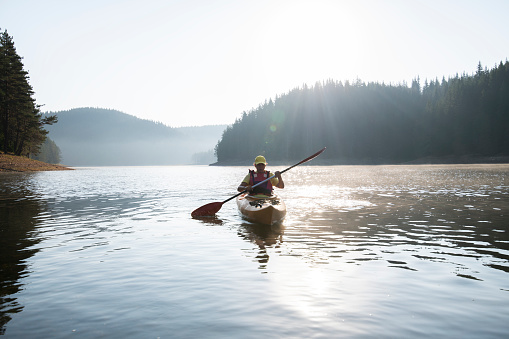A beautiful woman  rowing with kayak on sunrise light in mountain reflection lake.