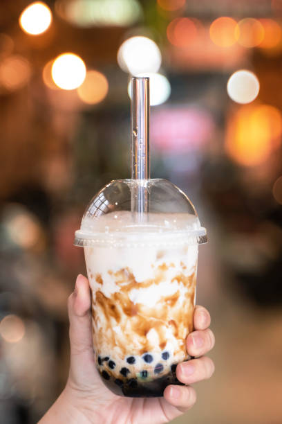 istock Young girl in denim jacket is drinking brown sugar flavored tapioca pearl bubble milk tea with glass straw in night market of Taiwan. 1170489801