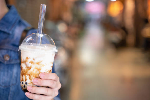 istock Young girl in denim jacket is drinking brown sugar flavored tapioca pearl bubble milk tea with glass straw in night market of Taiwan. 1170489822