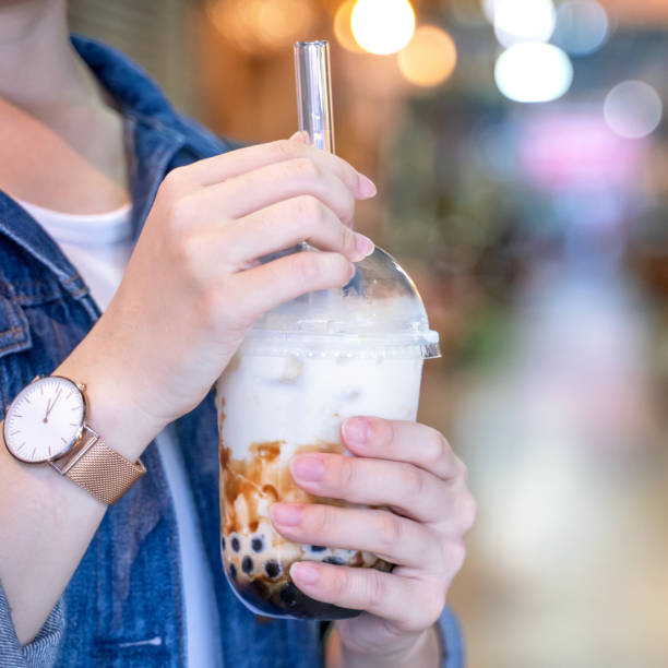 istock Young girl in denim jacket is drinking brown sugar flavored tapioca pearl bubble milk tea with glass straw in night market of Taiwan. 1170489849