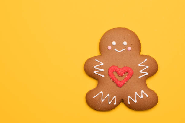 Christmas Gingerbread man sugar cookie in humanoid shape with red heart icing decoration on yellow background