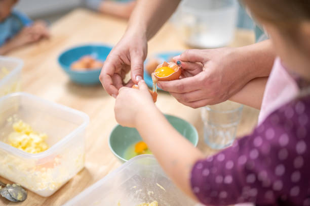 kobieta i dziewczyna łamiąc jajko na ciasteczka - on eggs standing spoon zdjęcia i obrazy z banku zdjęć