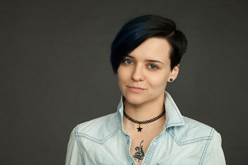 Studio portrait of an attractive 30 year old woman with blue hair in a jeans shirt on a black background