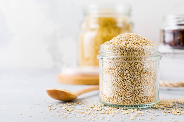 Raw quinoa grains in jar. Healthy vegetarian food on gray kitchen table. Selective focus. stock photo