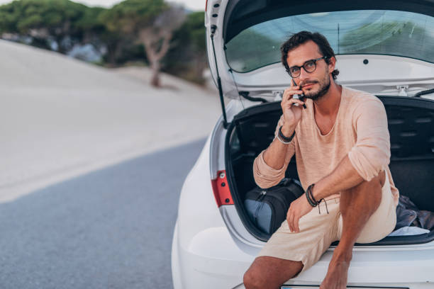 istock Man sitting on car trunk and talking on phone 1170496036
