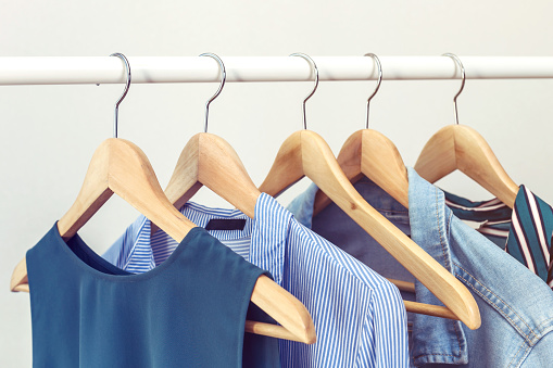 Collection of clothes hanging on rack near white wall. Clothes for women in blue colors. Office Style.