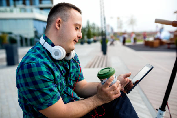 Teen boy with Down syndrome on the way to school Young man student with Down syndrome riding an electric scooter in a city and listening to the music assistive technology stock pictures, royalty-free photos & images