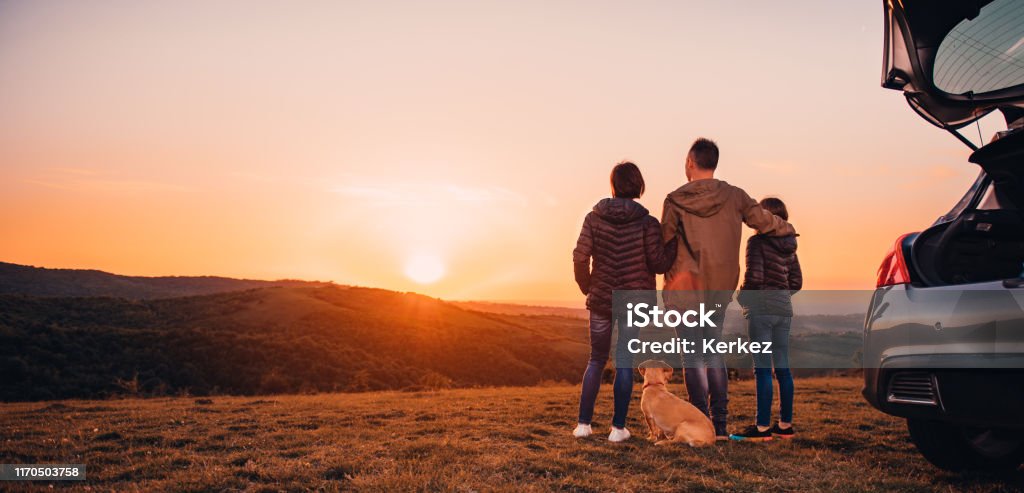 Famiglia con cane che si abbraccia in collina e guarda il tramonto - Foto stock royalty-free di Famiglia