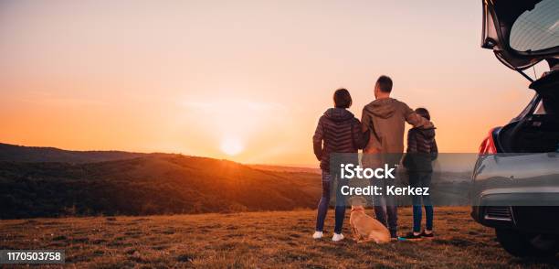 Famiglia Con Cane Che Si Abbraccia In Collina E Guarda Il Tramonto - Fotografie stock e altre immagini di Famiglia