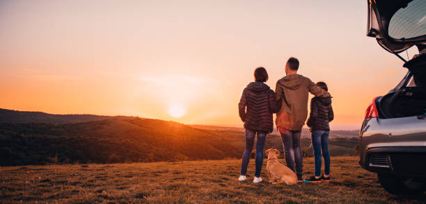 Family with small yellow dog embracing at hill and looking at sunset