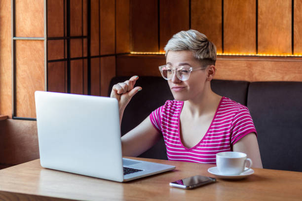 ein wenig! porträt von attraktiven jungen mädchen mit kurzen haaren in rosa t-shirt sitzt im café, arbeiten und machen videoanruf auf laptop, erfreut ihren begleiter, mehr zeit zu geben - pleading women business sadness stock-fotos und bilder