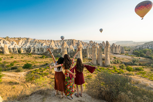 Balloons burning fuel as they fly over the city of Goreme in Cappadocia, with sightseeing tourists during a sunny summer day